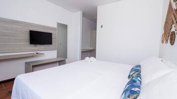 Quarto de hotel com cama, televisão de tela plana na parede e prateleira de madeira.