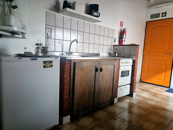 A kitchen with a refrigerator, stove, sink, and a coffee maker on a shelf.