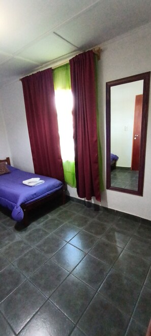 Una habitación con cama, espejo y ventana con cortinas.