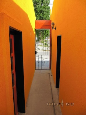 A narrow corridor with orange walls, a metal gate, and a red door.
