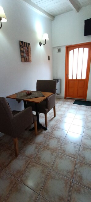 Un comedor con una mesa de madera y dos sillas, una obra de arte en la pared y una puerta con ventanal.