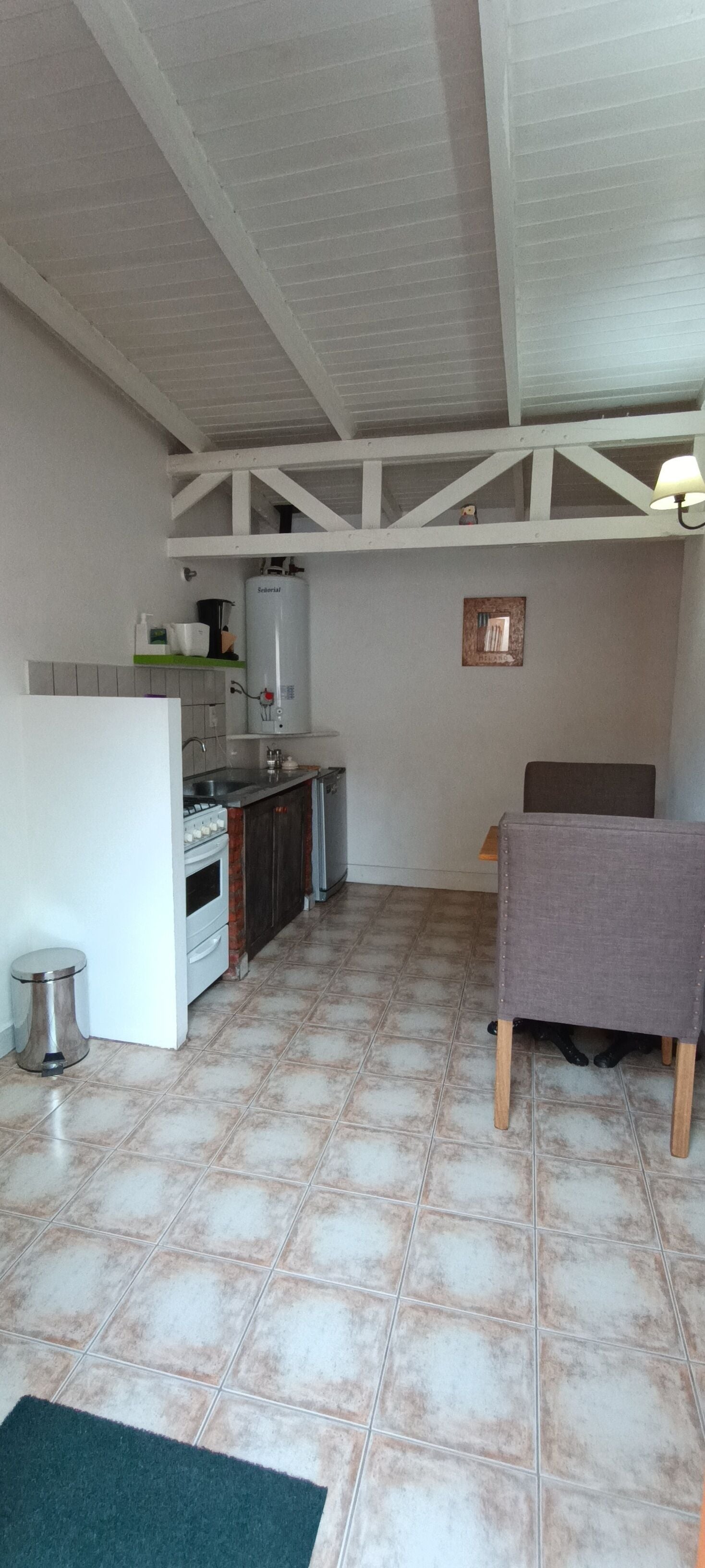 Una cocina compacta con estufa a gas, pileta e calentador de agua. Hay una zona de comedor con una mesa y sillas.