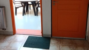 Un espacio interior con piso de baldosas, una puerta naranja cerrada, un televisor montado en la pared y un cartel que indica una salida de emergencia.