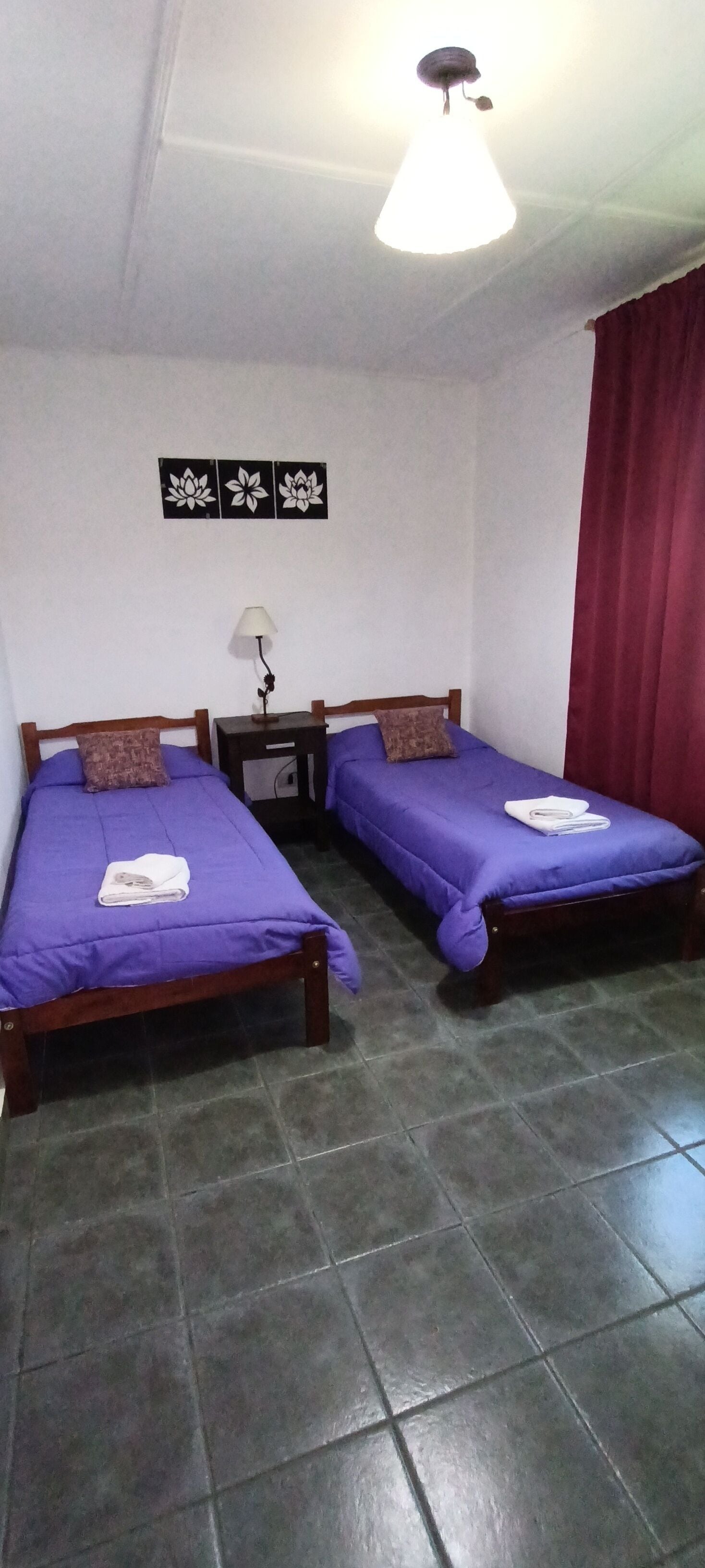 Habitació amb dos llits, una tauleta de nit, una làmpada i una cortina vermella.