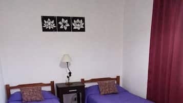 Une chambre avec deux lits, une table de chevet, une lampe et un rideau rouge.