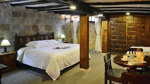 Een rustieke kamer met een stenen muur, een houten bed en een ronde tafel met een stoel.