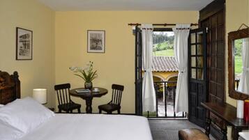 Una habitación de hotel con una cama, una mesa con sillas, un florero y vistas al exterior a través de una puerta abierta.