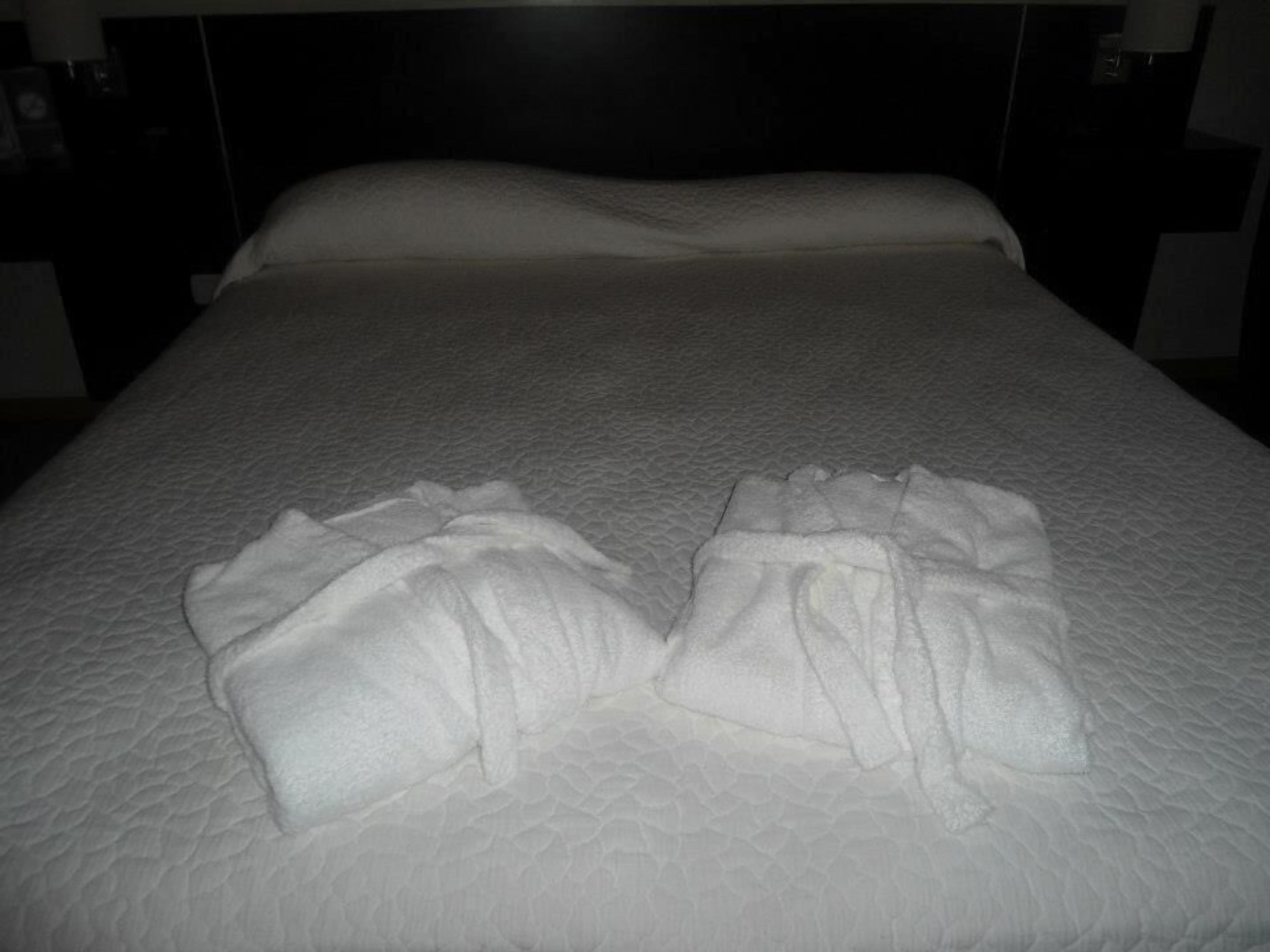 A neatly made bed with a textured white duvet and two folded towels on the bed.