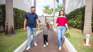 Uma família caminhando por um caminho pavimentado, com palmeiras e um edifício ao fundo.