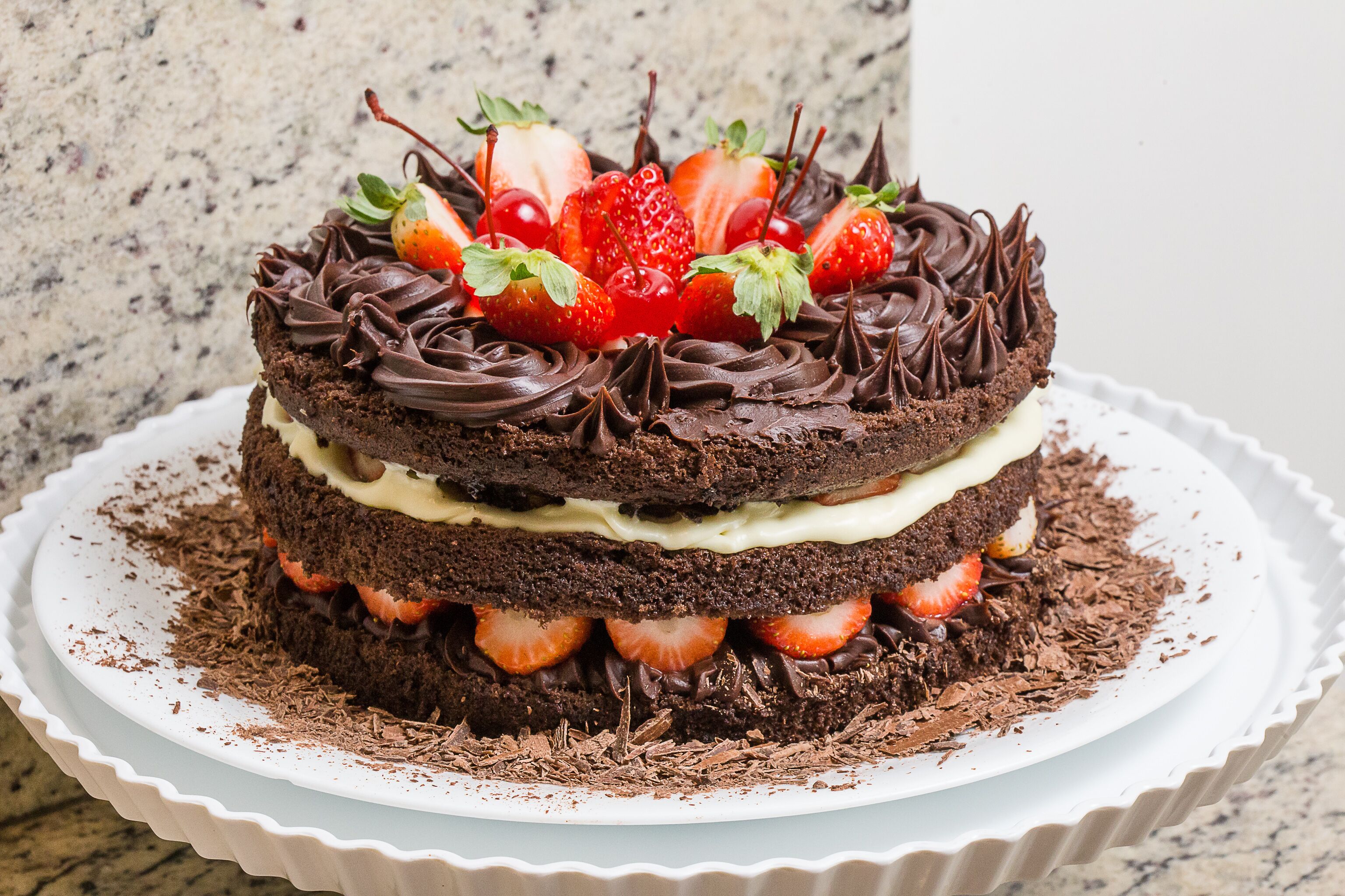 Un pastel de chocolate con varias capas, fresas y crema sobre un plato blanco.