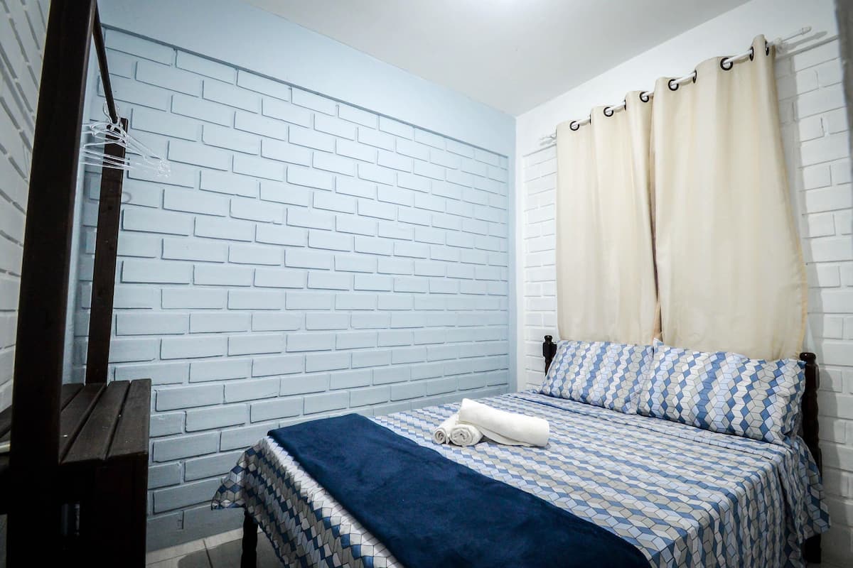 A bedroom with a brick-patterned wall, a bed with patterned bedding, a wooden nightstand, and a hanging light fixture.