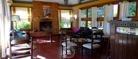 A spacious living room with a fireplace, wooden furniture, and large windows.