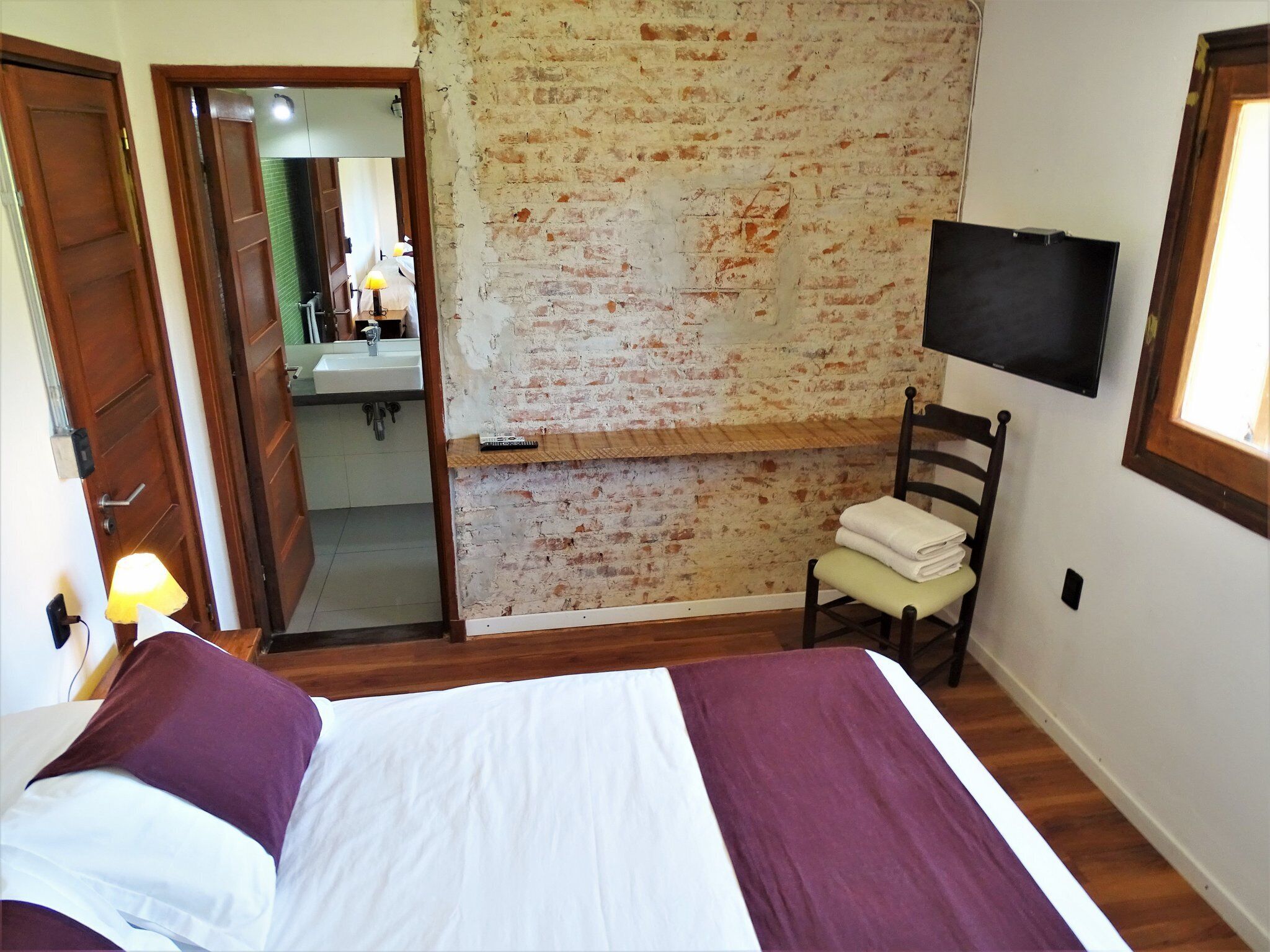 A bedroom with a bed, a chair, a television, and a brick wall.