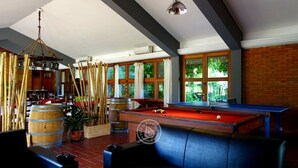 A billiards room with a pool table, leather seating, and large windows. - Hosteria del Pescador (Punta del Diablo)