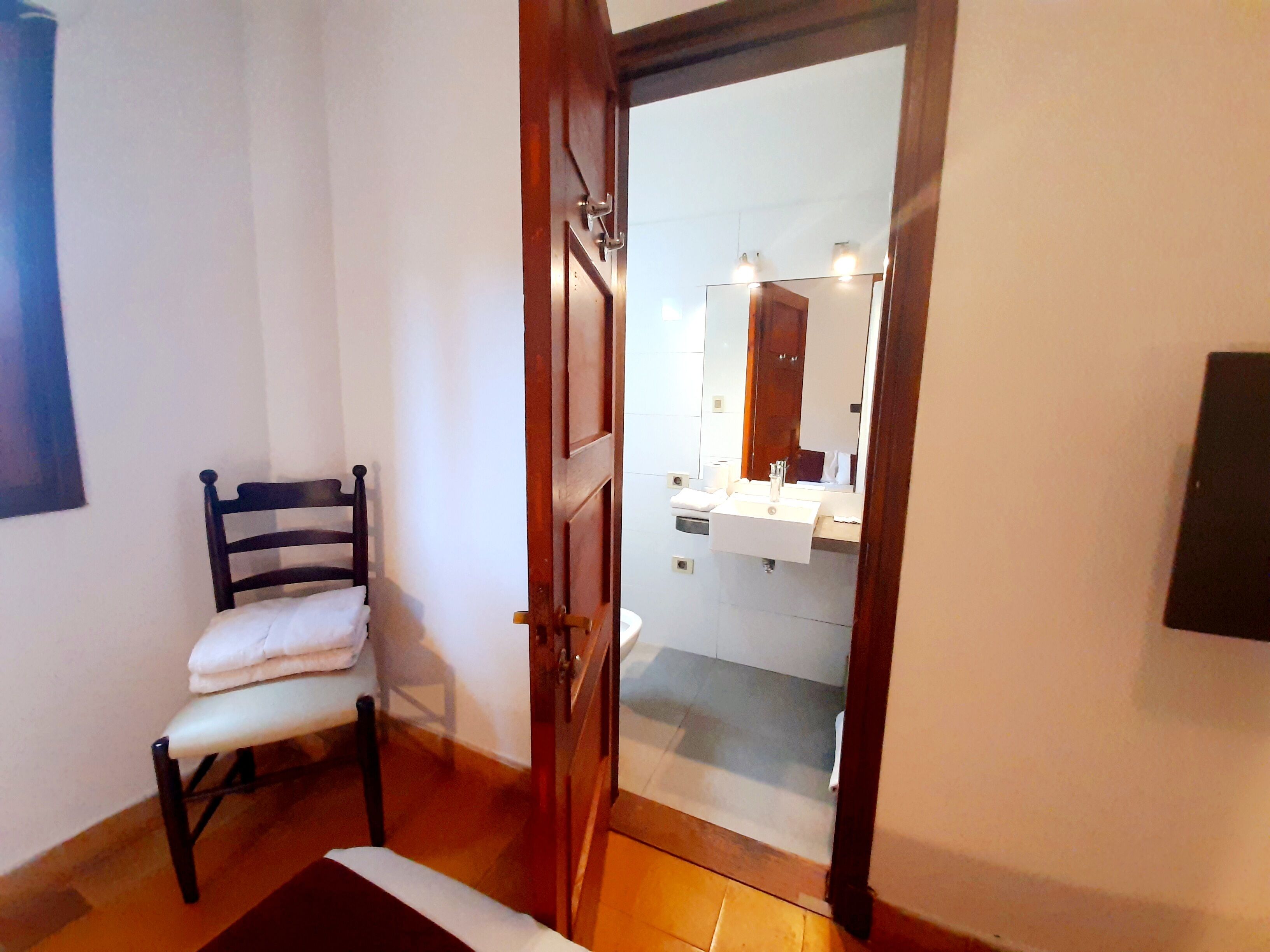 Un baño con puerta de madera, lavamanos blanco y espejo.