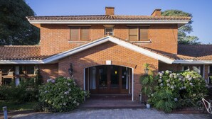 A brick building with a tiled roof, a central entrance with a glass door, and a small porch area. - Hosteria del Pescador (Punta del Diablo)