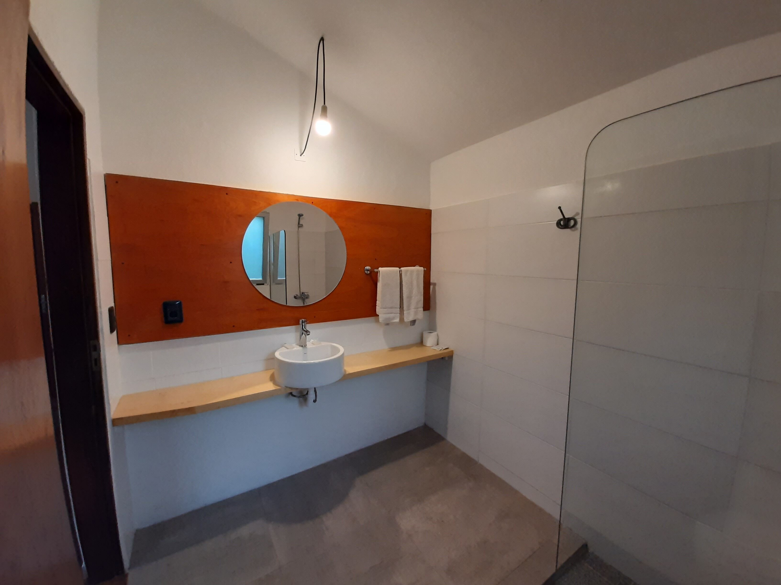 A bathroom with a round mirror, a sink, a towel rack, and a shower area.
