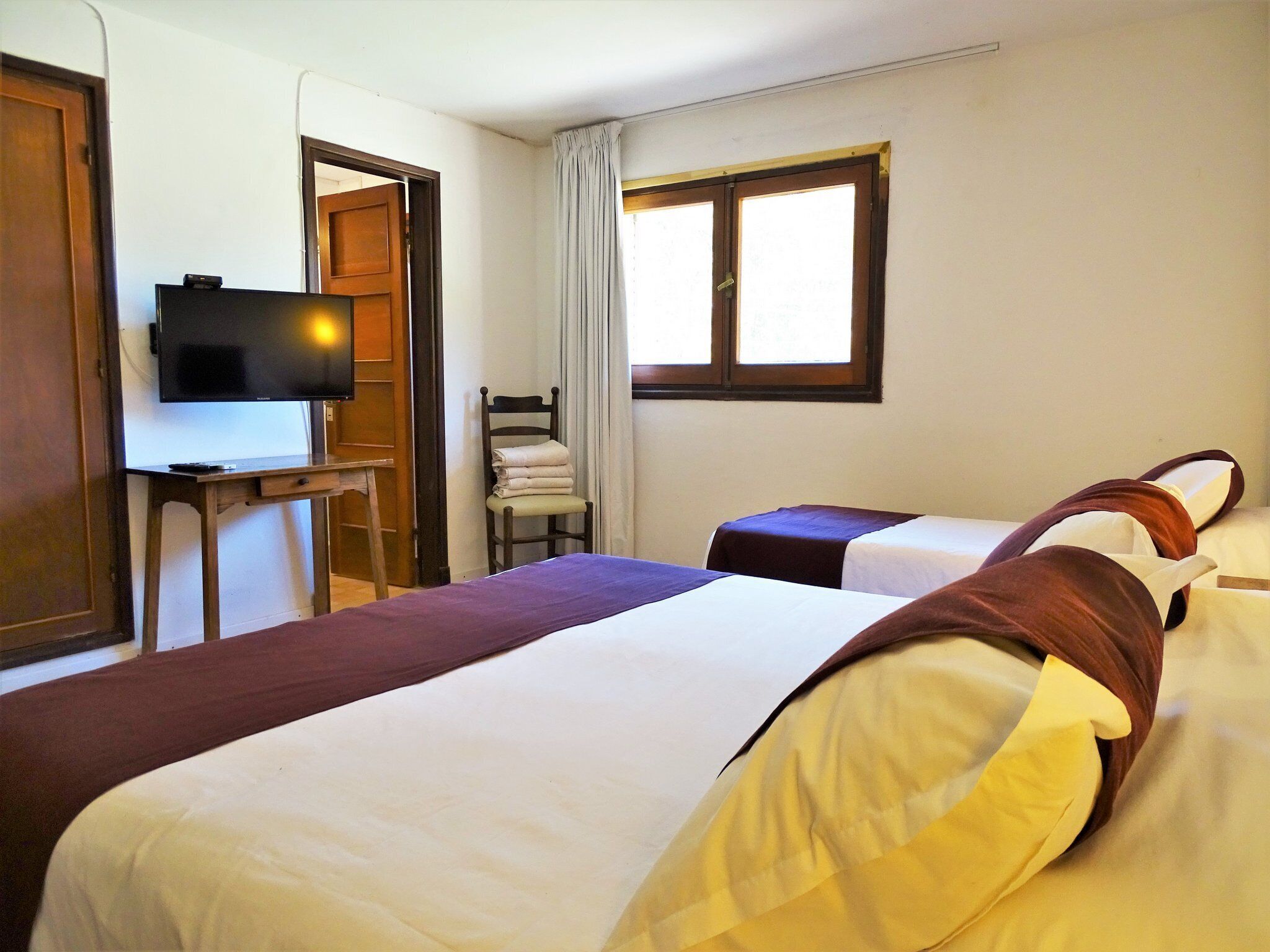 A hotel room with two beds, a TV, a desk, and a chair.