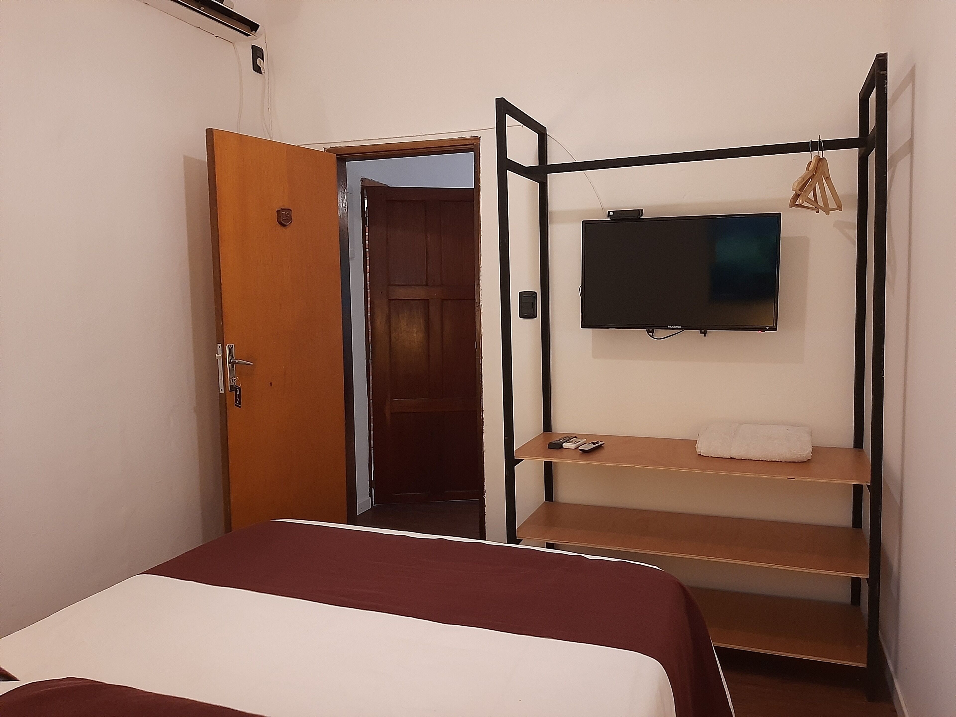 Una habitación de hotel con una cama, un televisor montado en un soporte de metal negro y una puerta de madera.