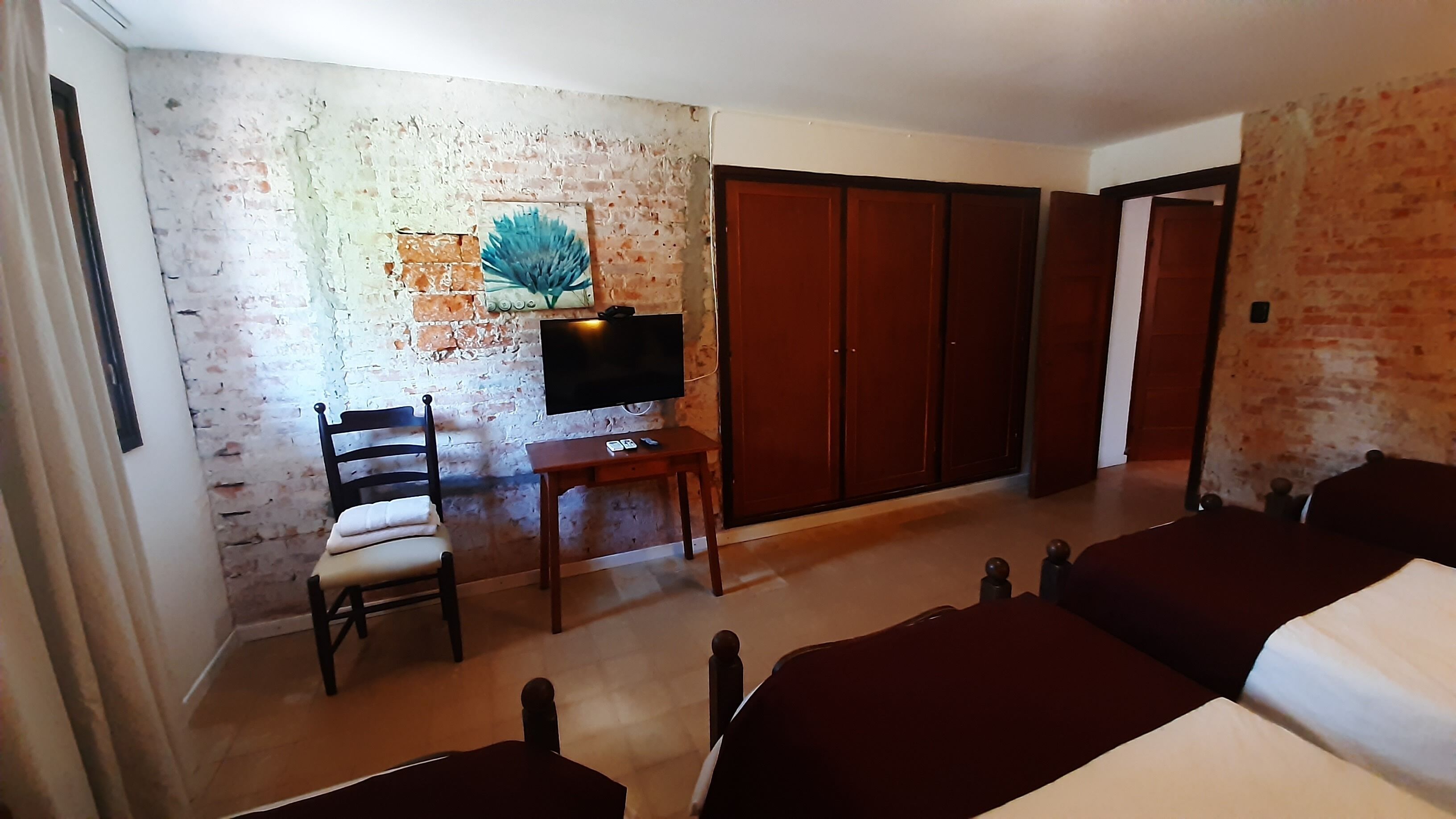 A room with a brick wall, a desk with a chair, a TV, and a wardrobe.