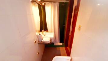 A narrow bathroom with a sink, toilet, and shower area.