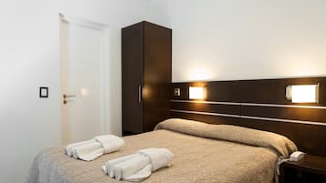 Una cama bien hecha con una colcha estampada y dos toallas enrolladas, un armario de madera oscura y un aplique de pared.