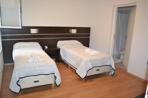 A room with two beds, each with a white bedspread and a pillow. There is a wooden floor and a dark headboard with wall-mounted lights. - Hotel del Sol (Córdoba)