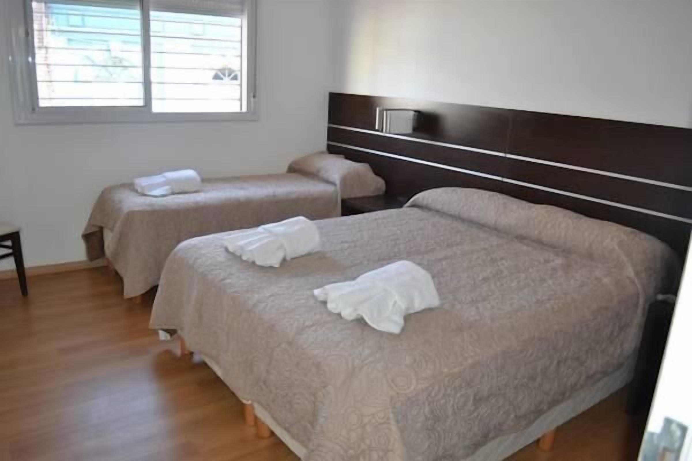 Habitación de hotel con dos camas, cada una con cabecera y almohada.