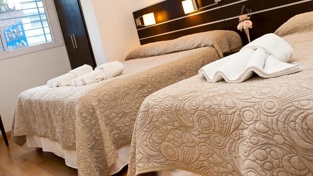 A hotel room with two beds, each with a patterned bedspread and a rolled white towel. - Hotel del Sol (Córdoba)