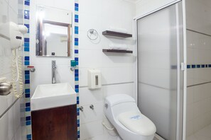 Un baño con lavamanos blanco, inodoro, espejo y zona de ducha.