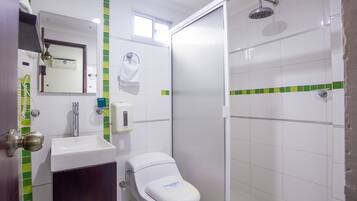 A bathroom with a white sink, a toilet, a mirror, a shower, and green-tiled walls.