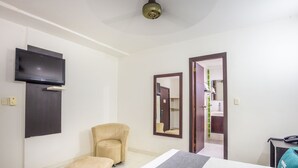 Une chambre d’hôtel avec un lit, un téléviseur fixé au mur, une chaise, un miroir et une salle de bain visible à travers une porte ouverte.