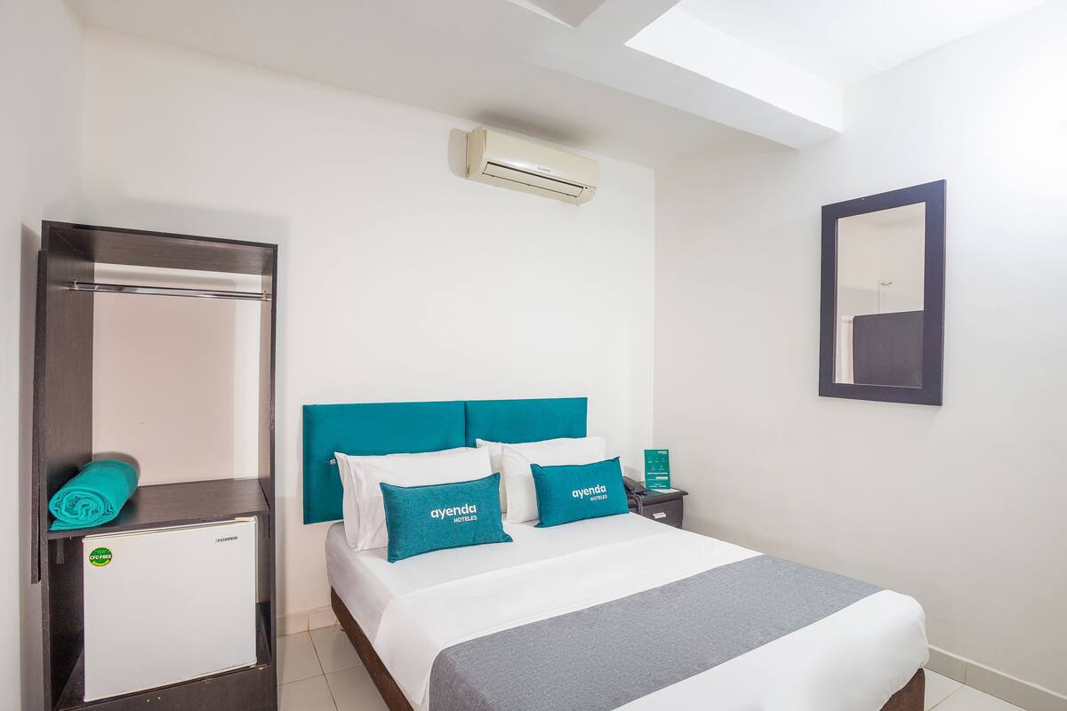 Une chambre d’hôtel équipée d’un lit, d’une table de chevet, d’un miroir et d’un climatiseur fixé au mur.