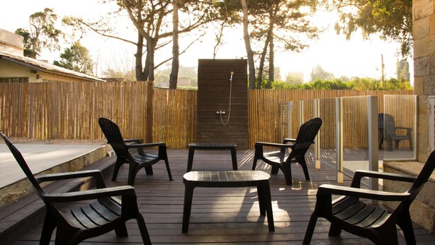 An outdoor seating area with four chairs and a table, surrounded by a wooden fence and trees. - Agostina´s (Valeria del Mar)