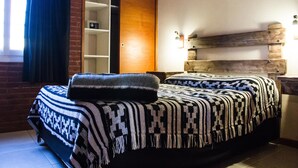 A bedroom with a bed covered in patterned blankets, a wooden headboard, a brick wall, and a sliding door closet. - Agostina´s (Valeria del Mar)