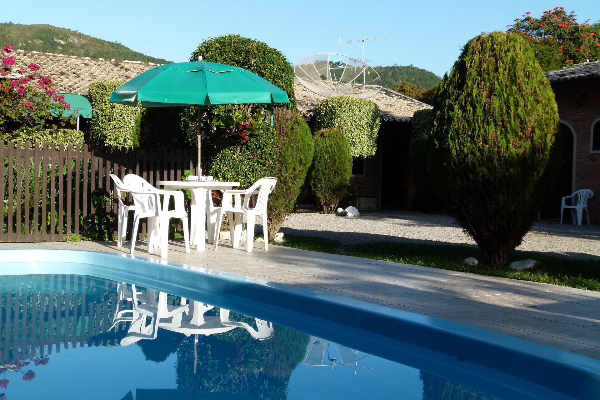 A swimming pool with a green umbrella, white plastic chairs, and a table.