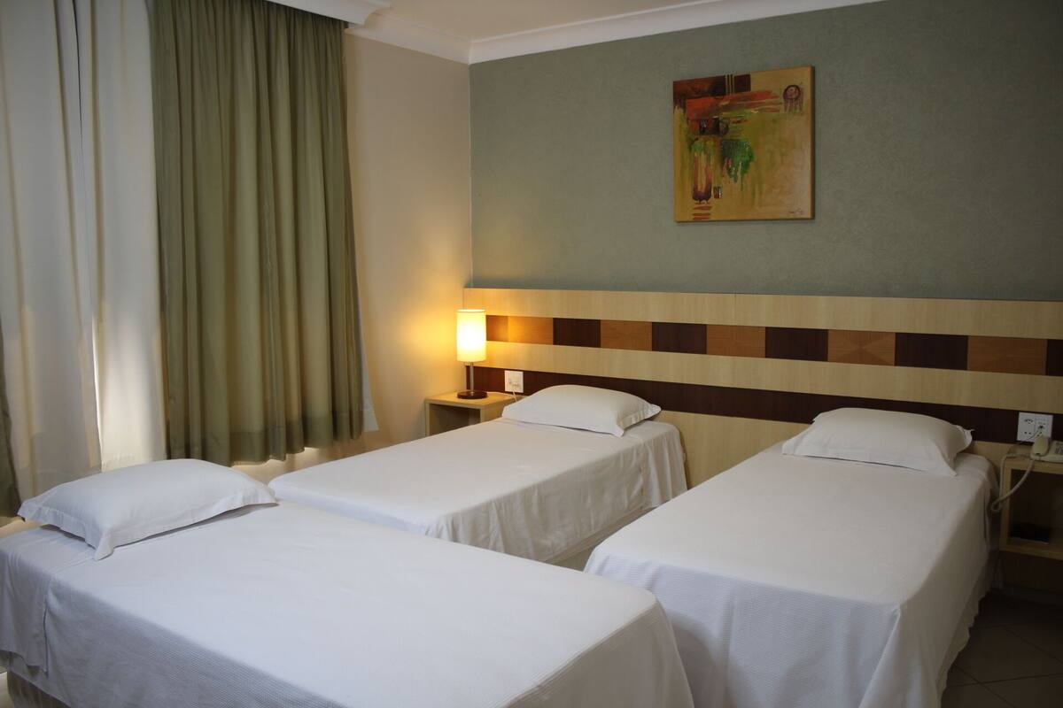 Habitación de hotel con dos camas individuales, una mesita de noche con lámpara, un cuadro en la pared y un teléfono sobre la mesita.