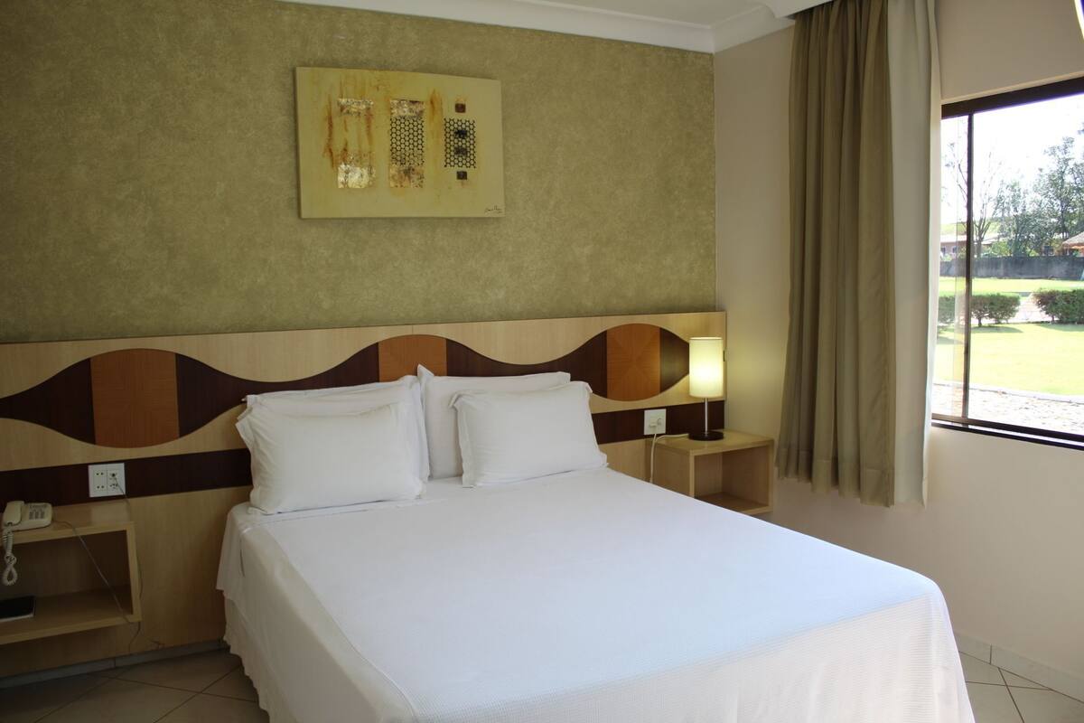Habitación de hotel con cama, mesita de noche con lámpara, teléfono y una obra de arte colgada en la pared.