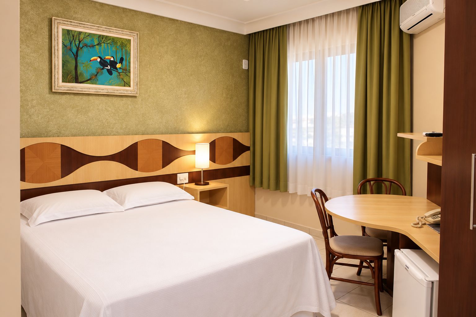 A hotel room with a bed, a desk with a chair, a painting on the wall, and a window with curtains.