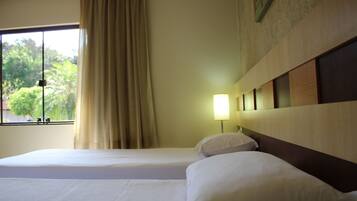 Habitación de hotel con dos camas, una ventana con cortinas, una lámpara de pared y vista a zonas verdes.