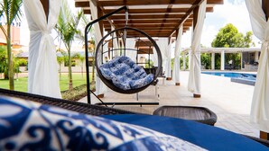 Un espace extérieur aménagé, abrité et doté de sièges, avec un fauteuil suspendu, une piscine et une vue sur le paysage environnant.
