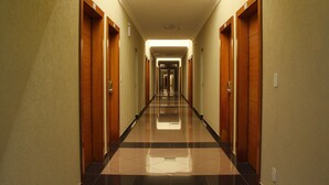 Un long couloir étroit, typique d’un hôtel, avec des portes en bois de chaque côté et un sol carrelé réfléchissant.