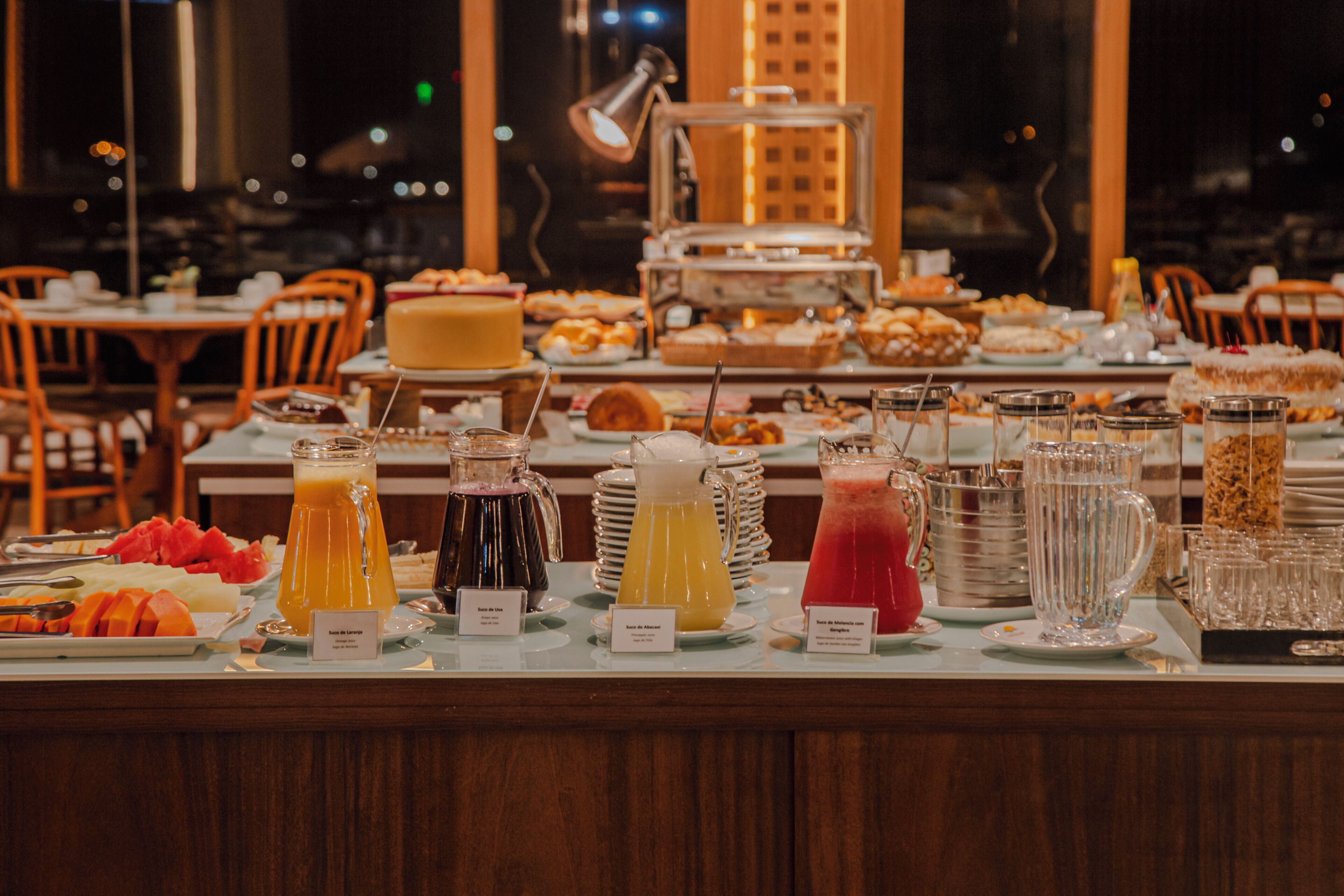 A buffet with various food and drink options, including fruits, juices, and a cake.