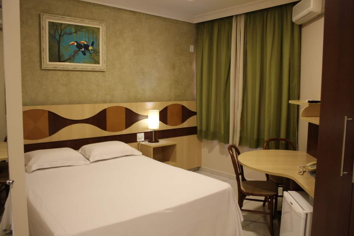 Habitación de hotel con cama, escritorio, silla, lámpara y un cuadro en la pared.