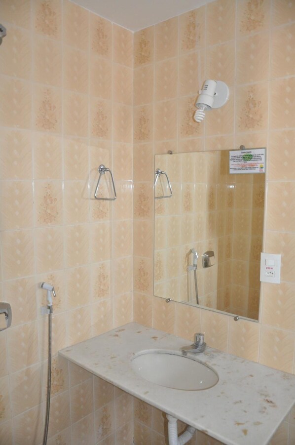 Un baño con baldosas beige con diseño, un lavamanos blanco, un espejo, un perchero para toallas y un cabezal de ducha.