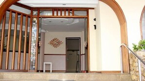 A residential entrance with a wooden gate, a small table, and a decorative wall piece. - Pousada Raio de Sol (Guarapari)