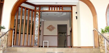 Entrada residencial com portão de madeira, uma pequena mesa e um detalhe decorativo na parede.