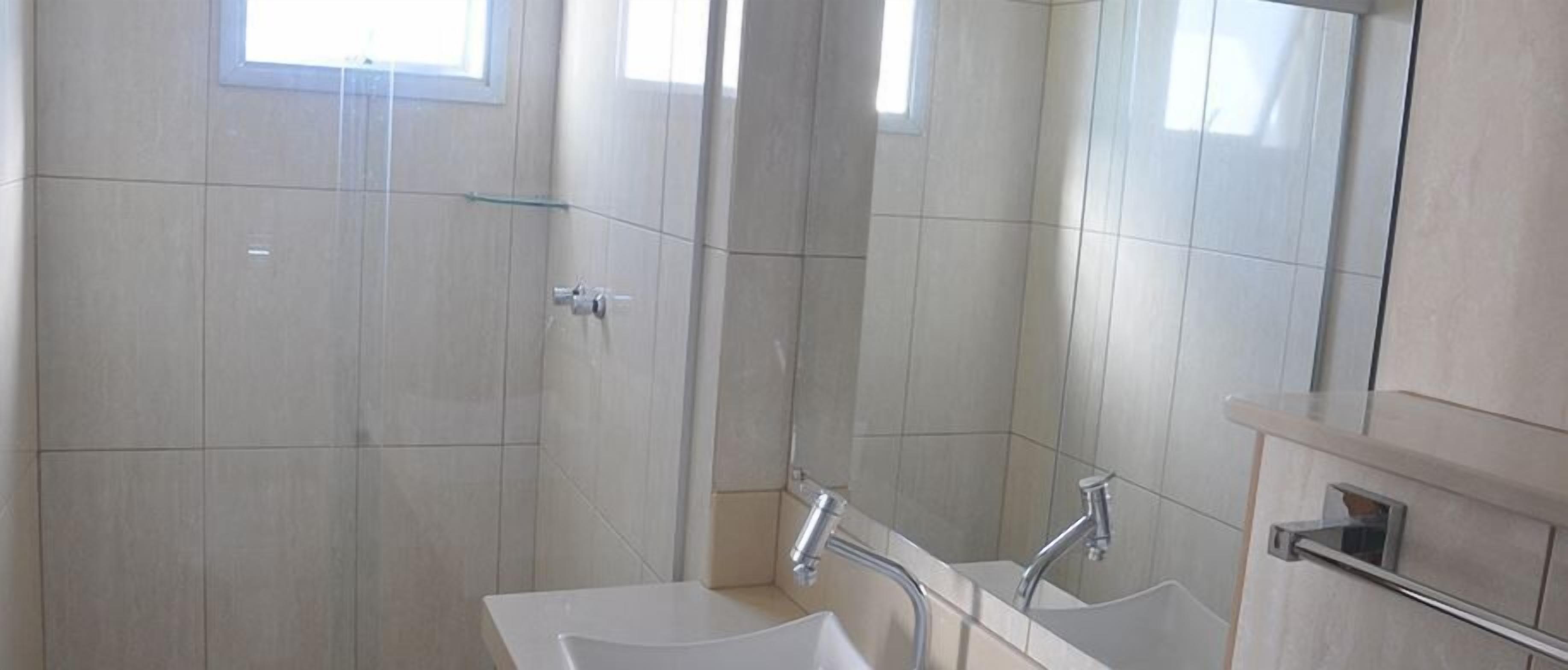 Un baño moderno con cabina de ducha de vidrio, un lavamanos con espejo y un mueble de tocador con toallero.