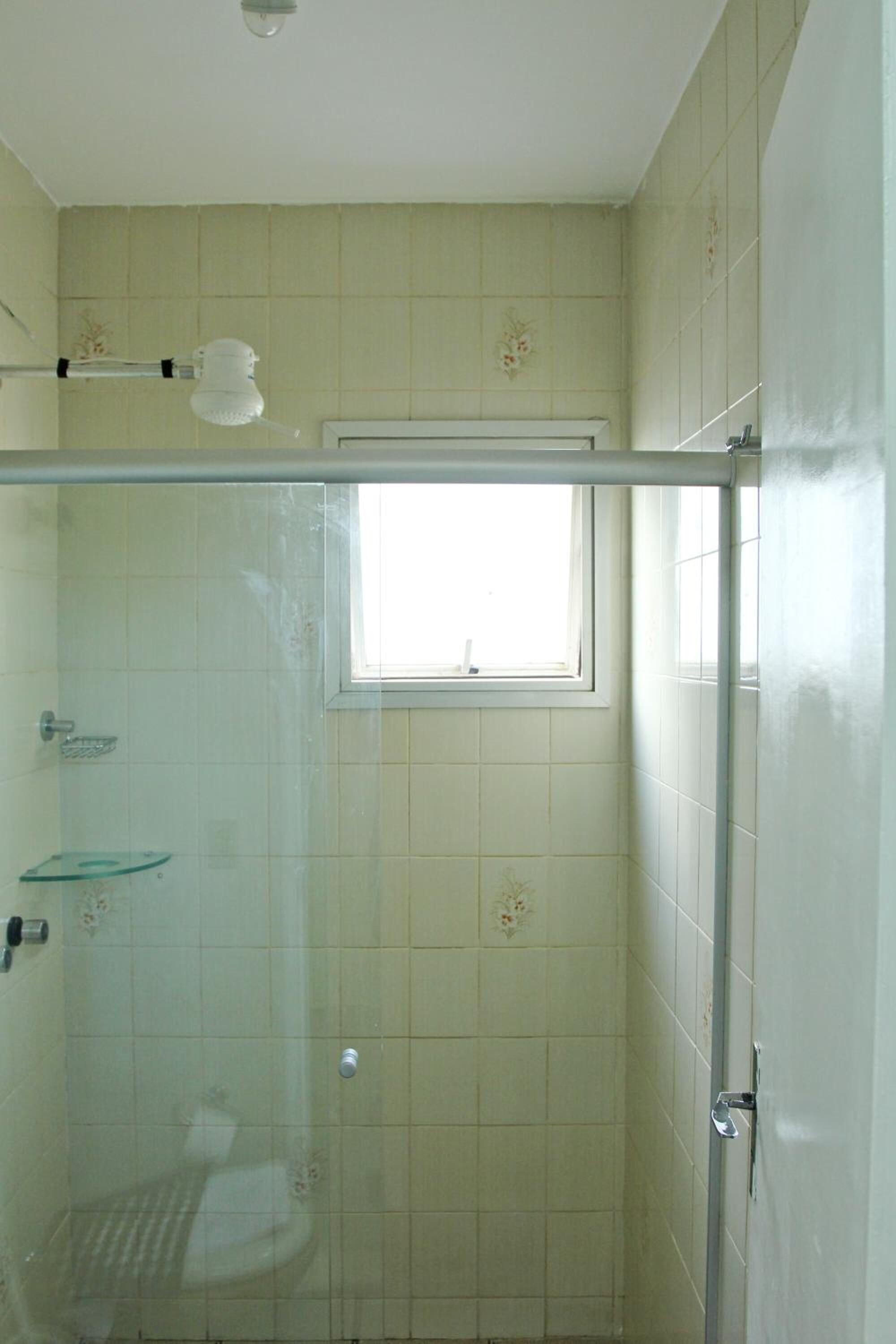 Une salle de bain avec une douche à parois de verre, une petite fenêtre et des murs carrelés.