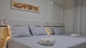 A neatly made bed with a white comforter and pillows, a wall-mounted artwork, and a bedside lamp. - Pousada Raio de Sol (Guarapari)